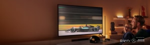 Pai e filho sorrindo enquanto assistem a uma corrida de carros de alta velocidade na TV, com iluminação inteligente da WiZ atrás da tela e nas prateleiras ao redor.