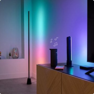 Un lampadaire dégradé, une barre lumineuse dégradée et un rétroéclairage TV, tous projetant une lumière synchronisée avec la musique diffusée par un haut-parleur dans un salon moderne.