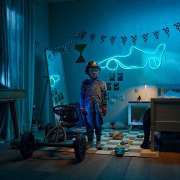Een jongetje staat naast een kart in zijn kamer met racethema, verlicht door een blauwe WiZ Smart Flex Strip in de vorm van een raceauto.